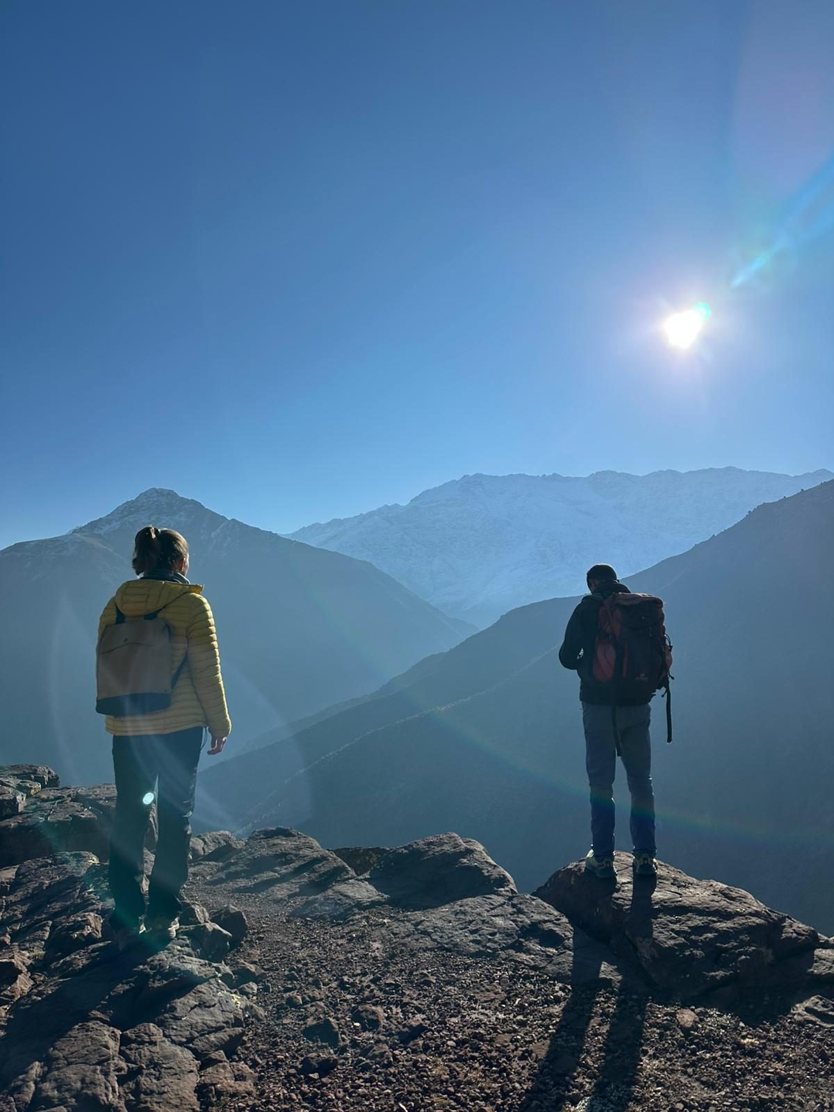 Two hikers looking out over snow-capped Atlas mountains